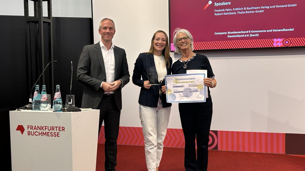 Eva Stütze, Geschäftsführerin von Autorenwelt, übergibt den symbolischen Check über 2.500 Euro an Huguette Morin-Hauser vom LESEMENTOR Bundesverband